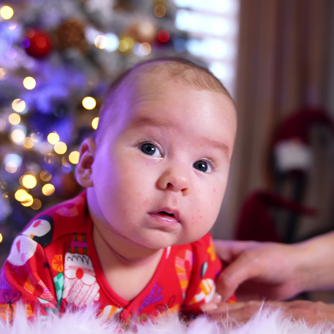 Beautiful Caucasian baby lies on the floor. Little boy is trying to hold his head and mommy supports the child