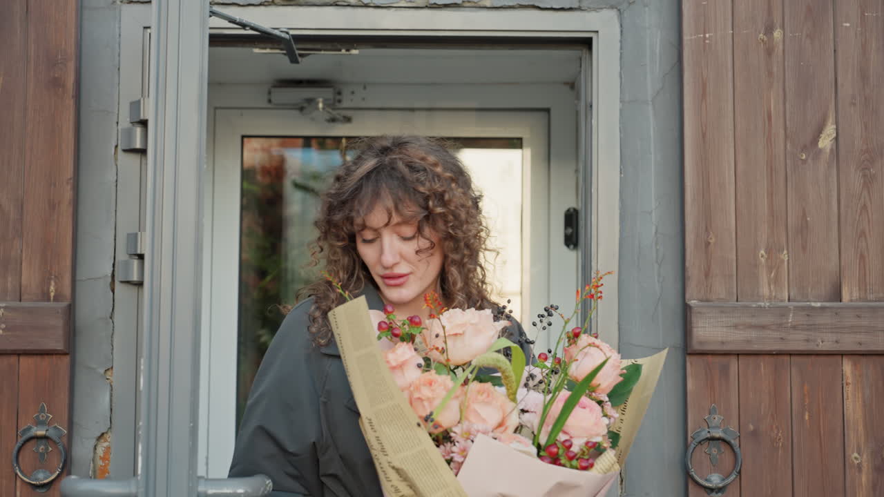 Florist arranging bouquet inside studio with peonies and greenery, caucasian artisan trimming stems and tying ribbon, rustic shelves and natural light highlight focused creative process