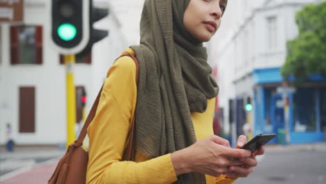 woman wearing hijab holding her phone in the street