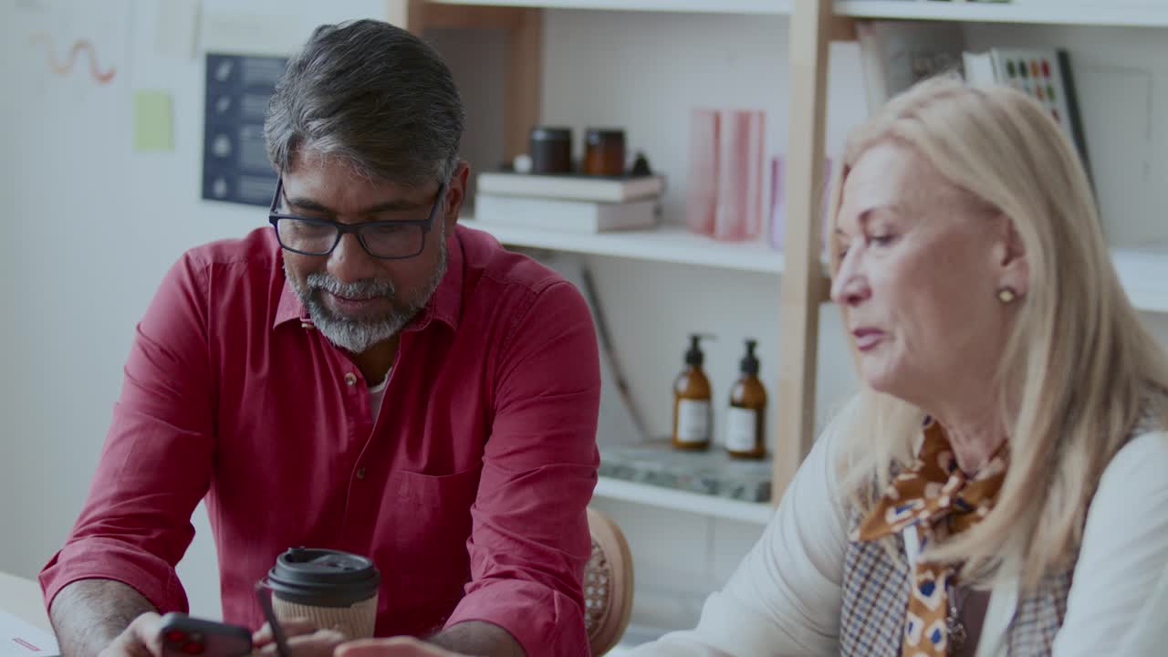 Senior Colleagues Discussing Data on Smartphone Screen in Office