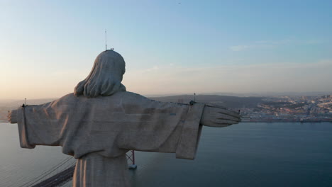 Drohnenkamera,-Die-Um-Die-Steinerne-Jesus-Statue-Herumfliegt.-Abendansicht-Von-Christ-The-King-Heiligtum-In-Almada-über-Tegus-Rives-In-Der-Untergehenden-Sonne.-Lissabon,-Hauptstadt-Von-Portugal.