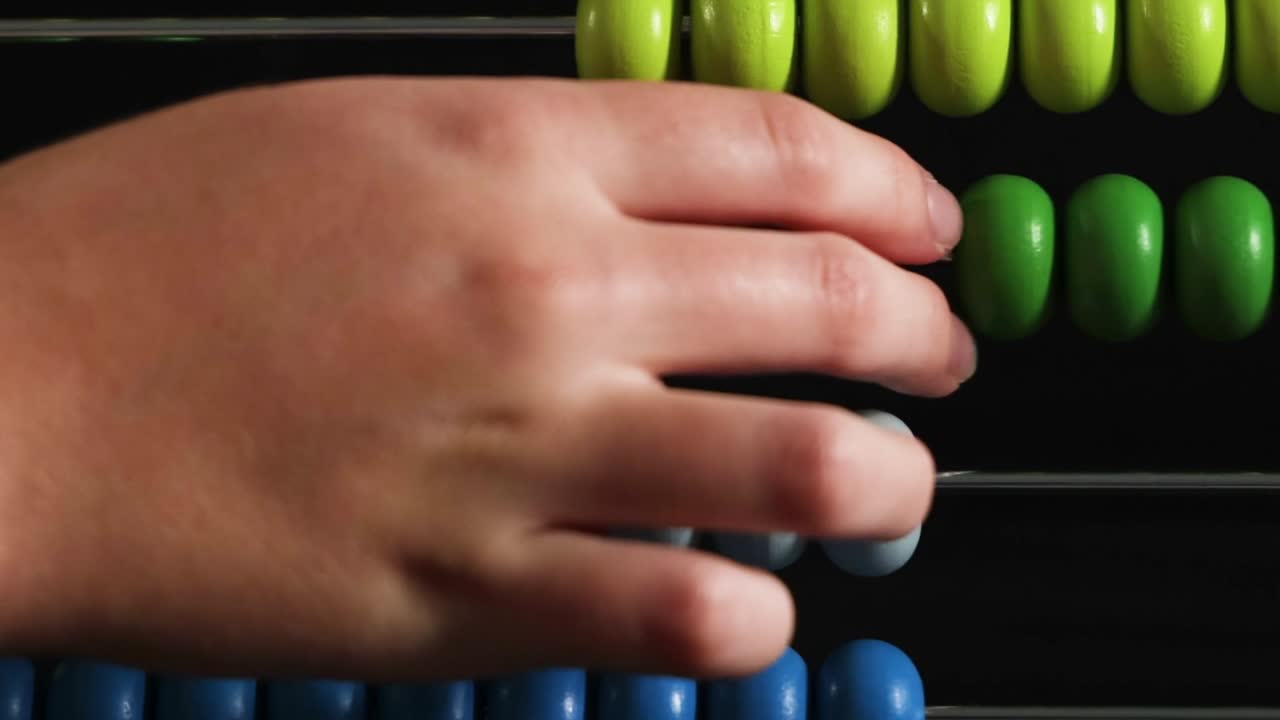 Close-up shot of a child's hand sliding colorful beads across an abacus against black background