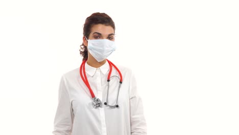 Portrait-of-a-female-doctor-looking-in-camera-and-taking-on-a-protection-mask.-Close-up-of-a-female-surgeon-with-stethoscope-and-lab-coat-isolated-on-white-background-dressing-up-surgical-mask