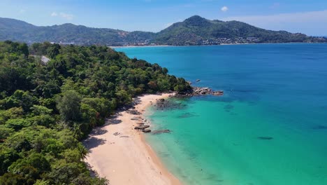 las imágenes aéreas capturan la serena belleza de la costa de phuket con aguas turquesas, exuberante vegetación y playas de arena bajo cielos despejados.