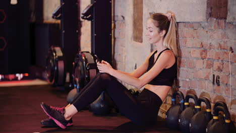 young athletic woman using mobile phone while resting during break at health club