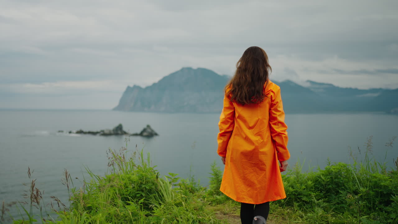 Woman in Orange Raincoat Exploring Coastal Scenery