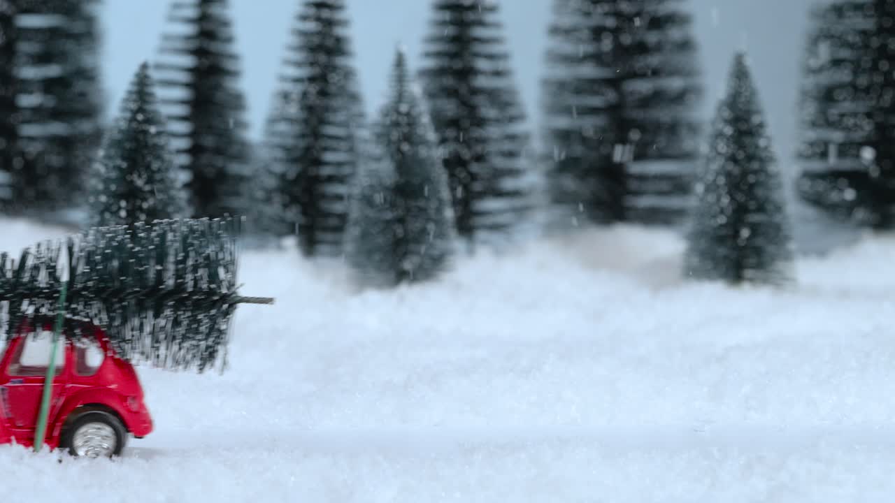 지붕에 크리스마스 트리가 있는 빨간색 장난감 자동차가 눈 인 숲을 따라 운전합니다. 오른쪽에서 왼쪽으로. 크리스마스 장식.