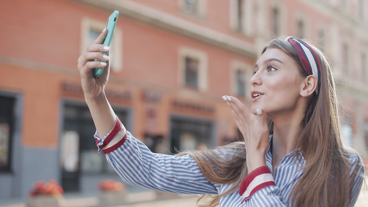 Jovem mulher feliz tirando uma selfie e mandando um beijo em uma rua da cidade.