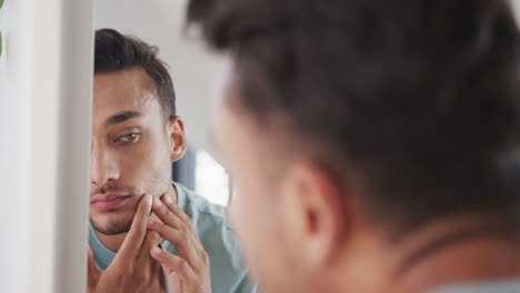 focused biracial man looking in bathroom mirror, examining his face and skin, slow motion