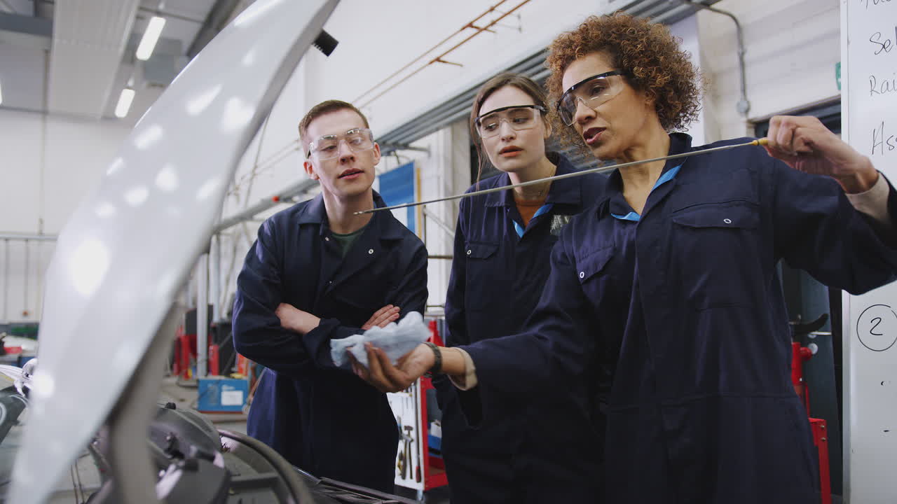 Female Tutor With Students Checking Oil Level In Car Engine On Auto Mechanic Course At College