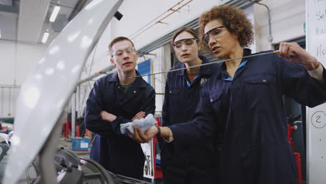 female tutor with students checking oil level in car engine on auto mechanic course at college