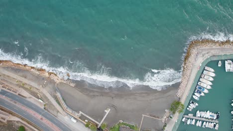 Toma-Aérea-De-Arriba-Hacia-Abajo-Del-Puerto-Deportivo-Con-Yates-Y-Olas-Que-Llegan-A-La-Playa-Del-Candado-En-Málaga