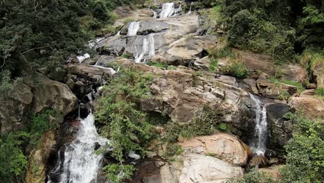 Aerial-Drone-Panning-Up-Cascading-Ravana-Falls-Waterfall-On-Rocky-Hillside-With-Lush-Green-Landscape-In-Ella-Sri-Lanka