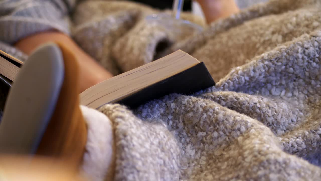 Alone time Hygge concept  - woman basking in cozy blanket and reading book in living room sofa, slider close shot
