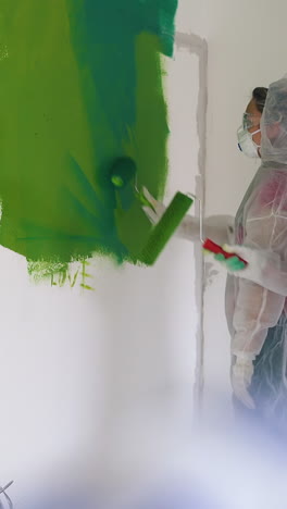 dolly cam shot: young people wearing white protective suits with masks come to white wall with color stain in renewing room