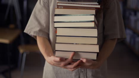 estudiante irreconocible camina con muchos libros en la biblioteca, preparándose para los exámenes