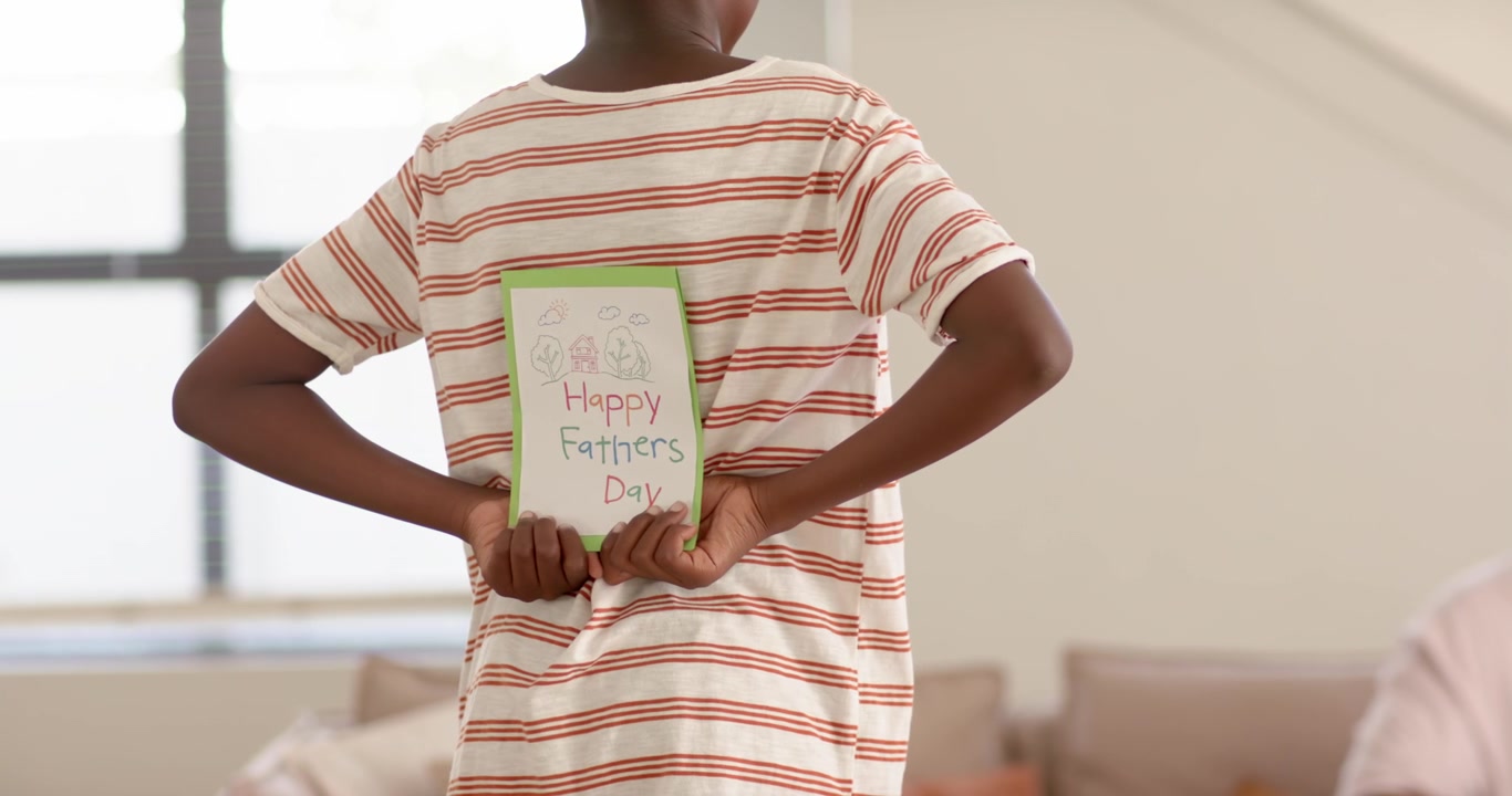 African American father, son revealing Fathers Day card, making father laugh with red phone on sofa