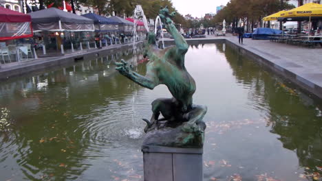 brussels fountain sculpture by green water canal in outdoor dining area with overcast sky