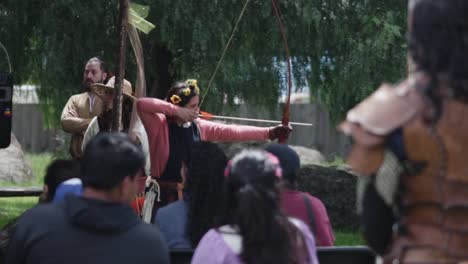 a group of people attend an outdoor medieval cultural event with costumed participants, a rustic setting surrounded by greenery.