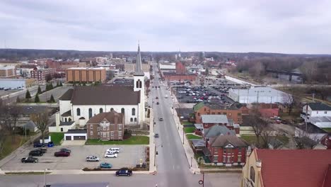 aerial view flyover logansport downtown street towards small white church with steeple in indiana townscape