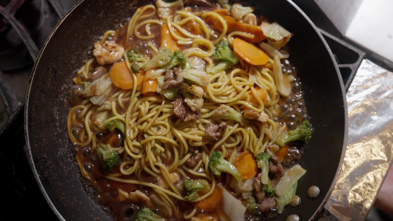 Tampilan luas pasta yang sedang dimasak dengan sayuran dan saus di wajan panas di atas kompor