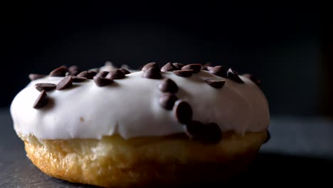 close-up circling around shot of delicious glazed white donut with chocolate chips spinning slowly on gray table background.