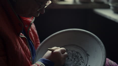 elderly woman making ornament on product in pottery. lady scraping in studio