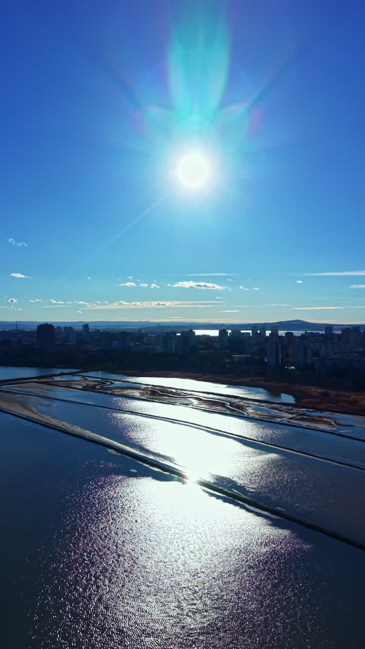 Bright sun shines over city and water with reflections in the afternoon sky and shoreline