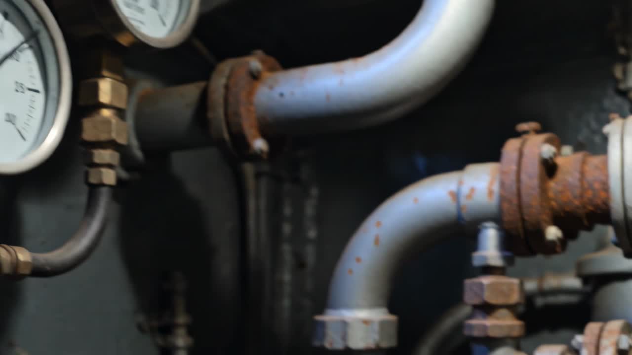 Telecamera che panoramica mostrando manometri e tubazioni su un pannello di controllo, mettendo a fuoco un collettore corroso