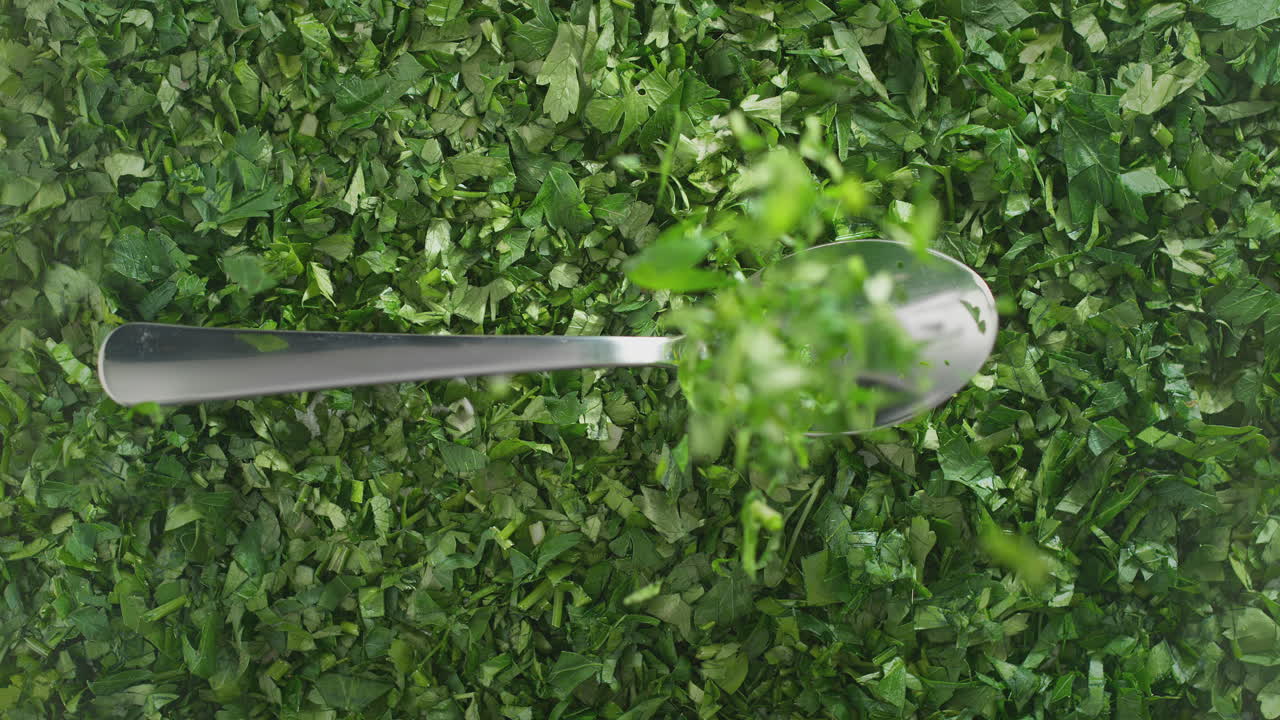 Silver Spoon With Chopped Parsley Falling Onto Green Seasonings - Top View