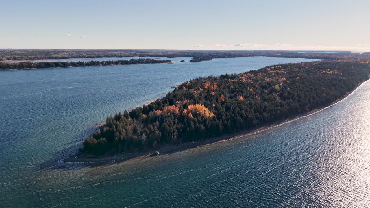 Aerial drone view of a forested peninsula stretching into a calm blue lake, with soft autumn hues and distant horizon
