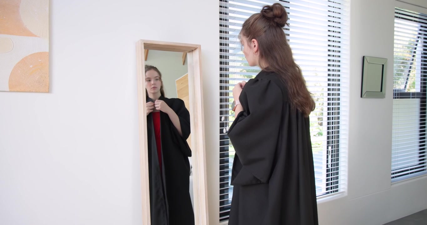 Donna adulta che controlla l'orologio, allaccia la vestaglia sopra un vestito rosso e si guarda allo specchio a casa per un evento
