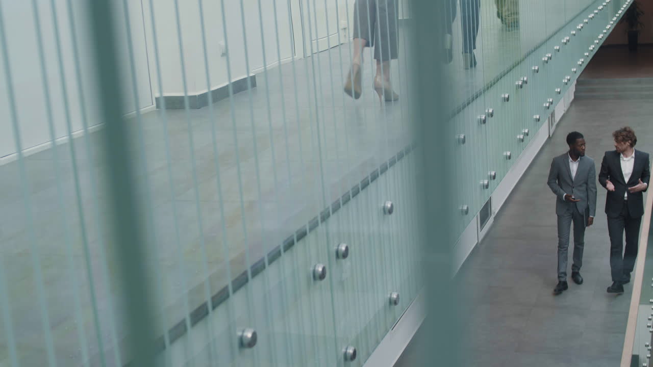 dos compañeros de trabajo masculinos yendo a lo largo del edificio de la oficina y hablando