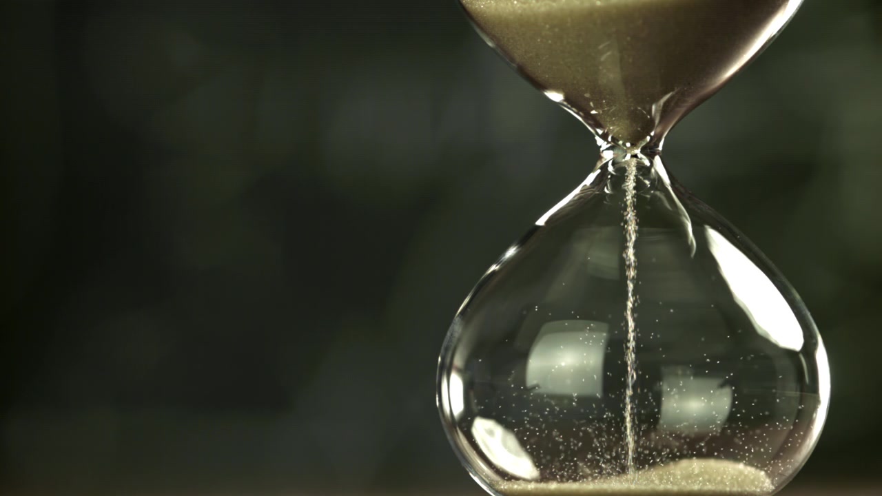 Sand Flowing Through a Classic Glass Hourglass, Symbolizing Time Passing