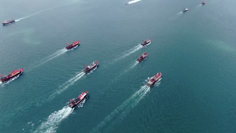 convoy of local fishing boats causing in hong kong victoria bay, with city skyline in the horizon, aerial view