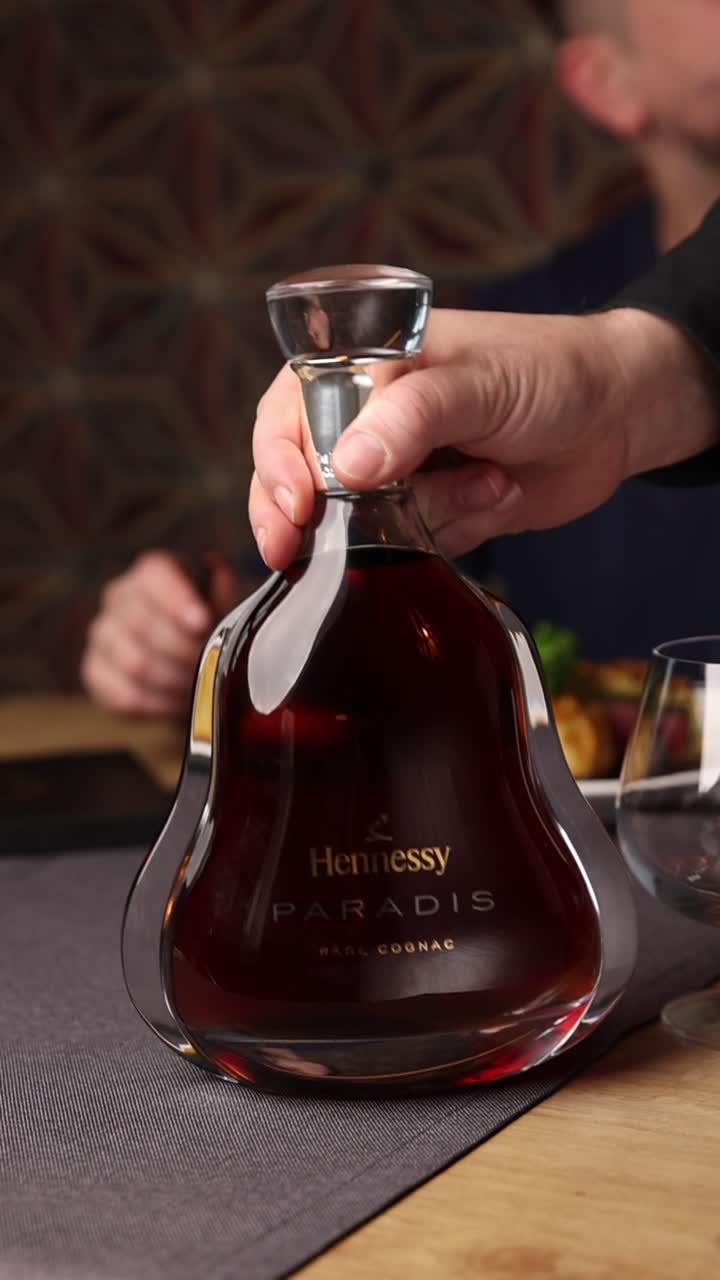 Mano che tiene una bottiglia di Hennessy Paradis Cognac in un ristorante di lusso