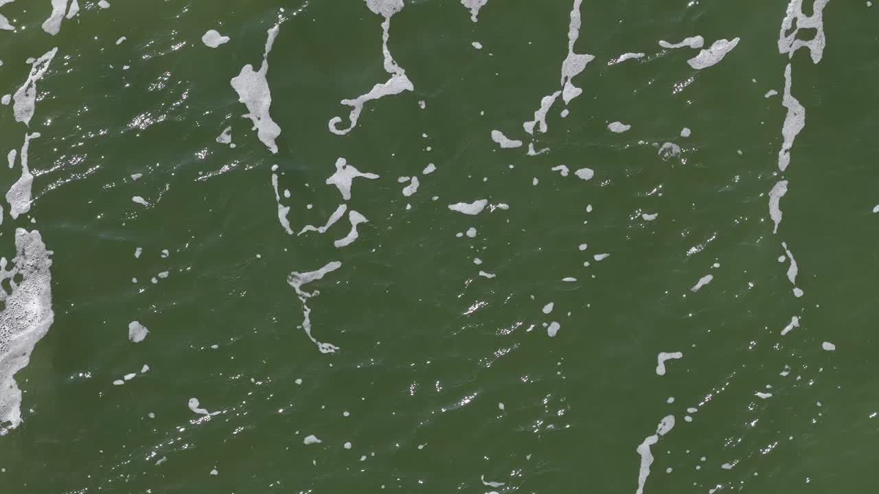 Overhead shot of green river water, white bubbles drifting, natural daylight, smooth camera movement