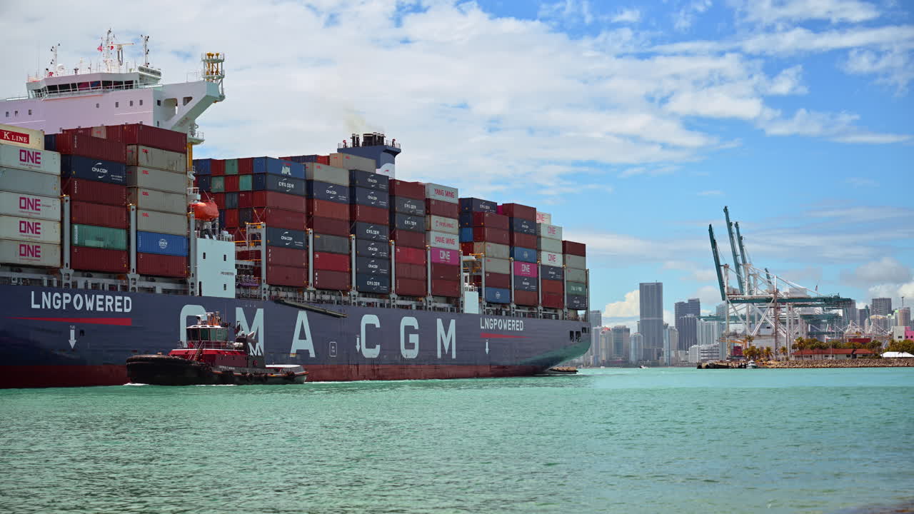 Miami, USA, 9 April 2026: Detail of container ship and tugboat at PortMiami. Close up view of a large cargo ship assisted by a red tugboat with the city skyline in the background