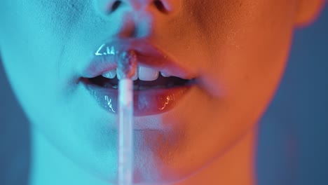 disparo de cerca de los labios de una hermosa mujer llena mientras la joven aplica brillo labial a sus labios para prepararse para la noche con contraste azul naranja en su cara en cámara lenta