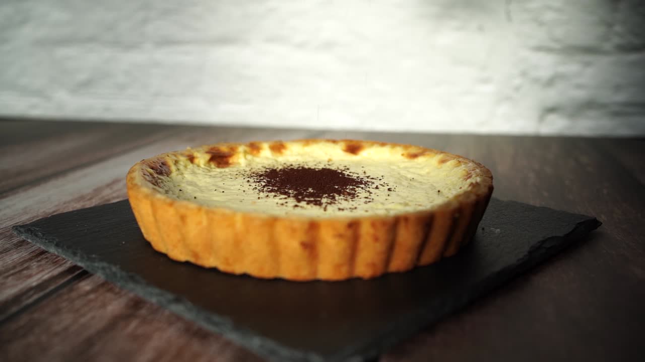 put cocoa powder on a crème brülée tart in slow motion.