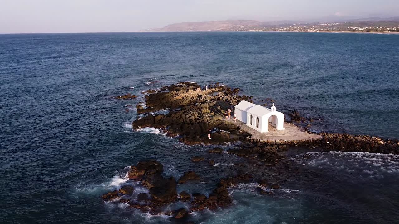 las olas del mar mediterráneo lavan la isla rocosa de una pequeña capilla, vista aérea