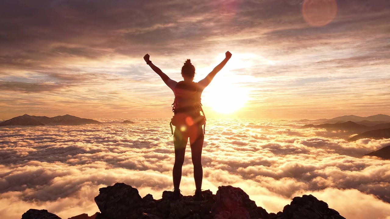 Ascesa trionfale: un escursionista celebra il viaggio della vita all'alba in cima a una maestosa vetta montuosa coperta di nuvole, bagnata da luce dorata