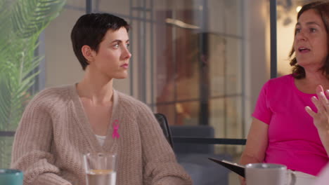 group of women wearing pink breast cancer awareness ribbons meeting and talking at therapy support group for cancer treatment patients 1