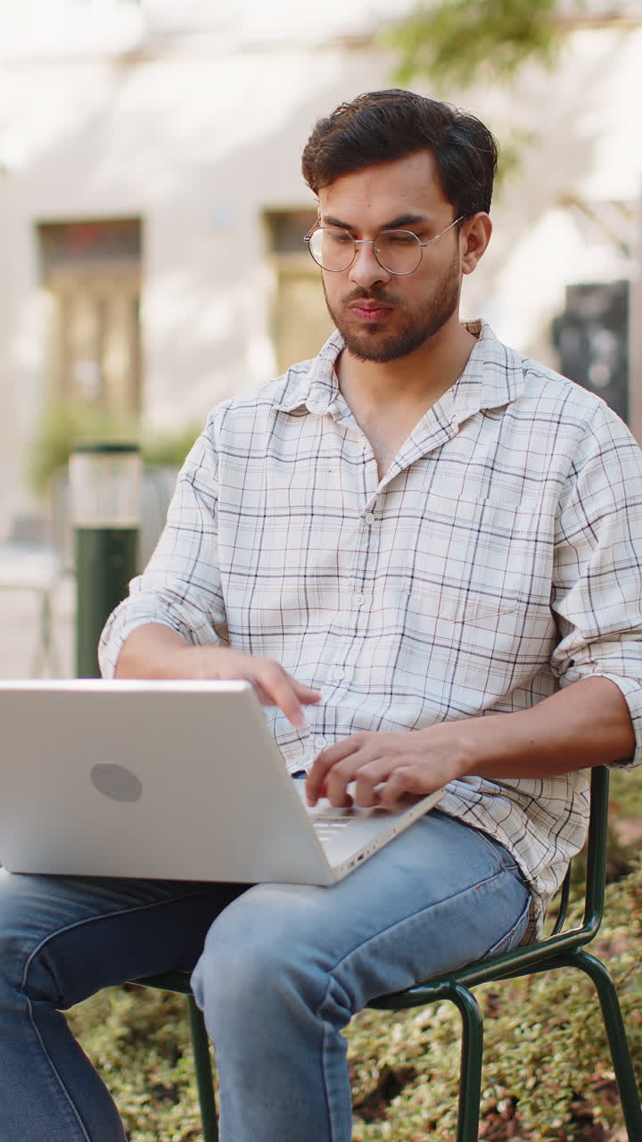 Indian man freelancer sitting on chair closes laptop screen finishing work smiling in city outdoors