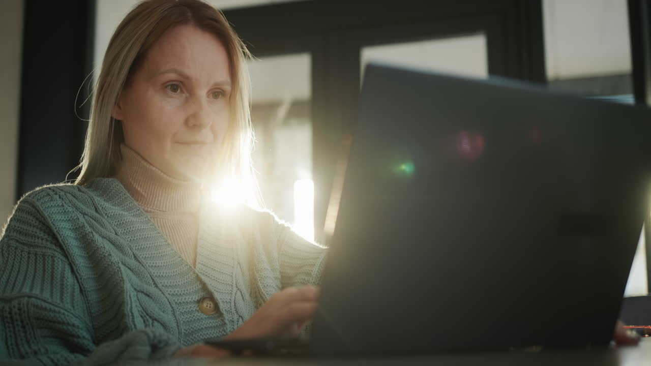 mujer de mediana edad usando una computadora portátil, el sol de la ventana la ilumina