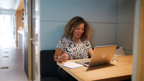 Nahaufnahme-Einer-Jungen-Frau-Gemischter-Abstammung,-Die-Allein-An-Einem-Laptop-An-Einem-Tisch-In-Einer-Kabine-In-Einer-Bürokantine-Arbeitet-Und-Redet-Und-Lächelt,-Vergrößerte-Aufnahme