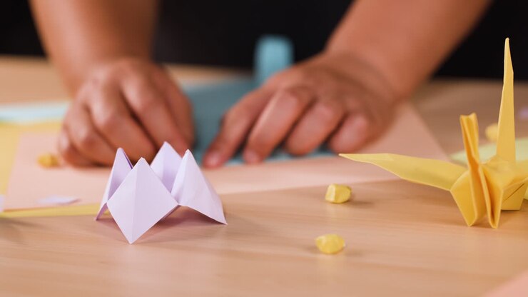 Close up shot of hands folding blue paper on a wooden table with origami figures