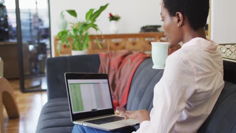 Happy-african-american-woman-sitting-on-sofa-in-living-room,-using-laptop