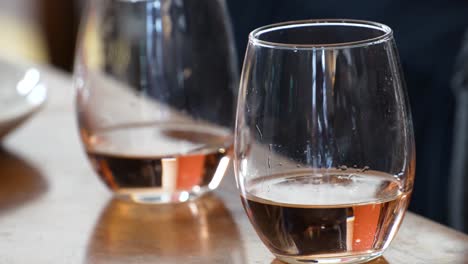 dos copas de vino sin tallo se sientan en una mesa de café llena hasta la mitad con vino rosado, un cierre de color rojo dorado con manchas y gotas de la bebida o bebida en el vaso