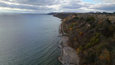a wide aerial dolly of a rocky coastal area with lush greenery and cliffs descending into the sea, calm waves lap on sandy shores